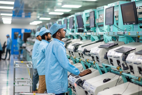 Noida, Uttar Pradesh, India- 11 Nov 2022: Factory workers in protective work gear seen working on mobile component manufacturing unit in Noida. look in at screen reading commands.